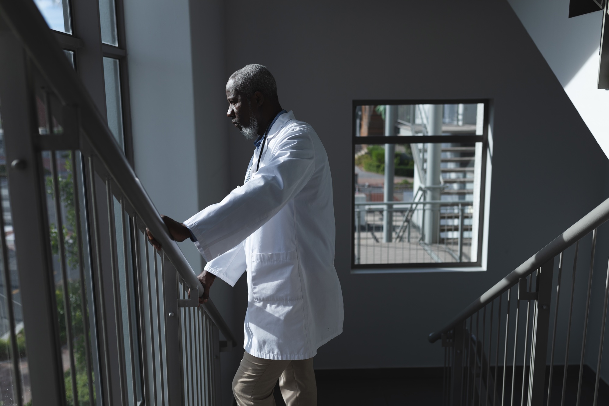 Portrait of african american male doctor looking through the window on hospital staircase